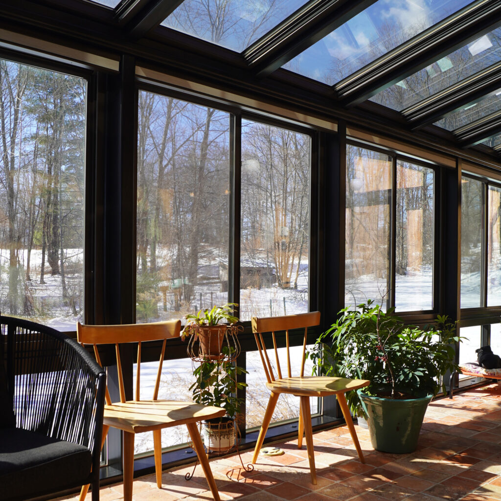 Interior shot of chairs, plants and windows in the sunroom.