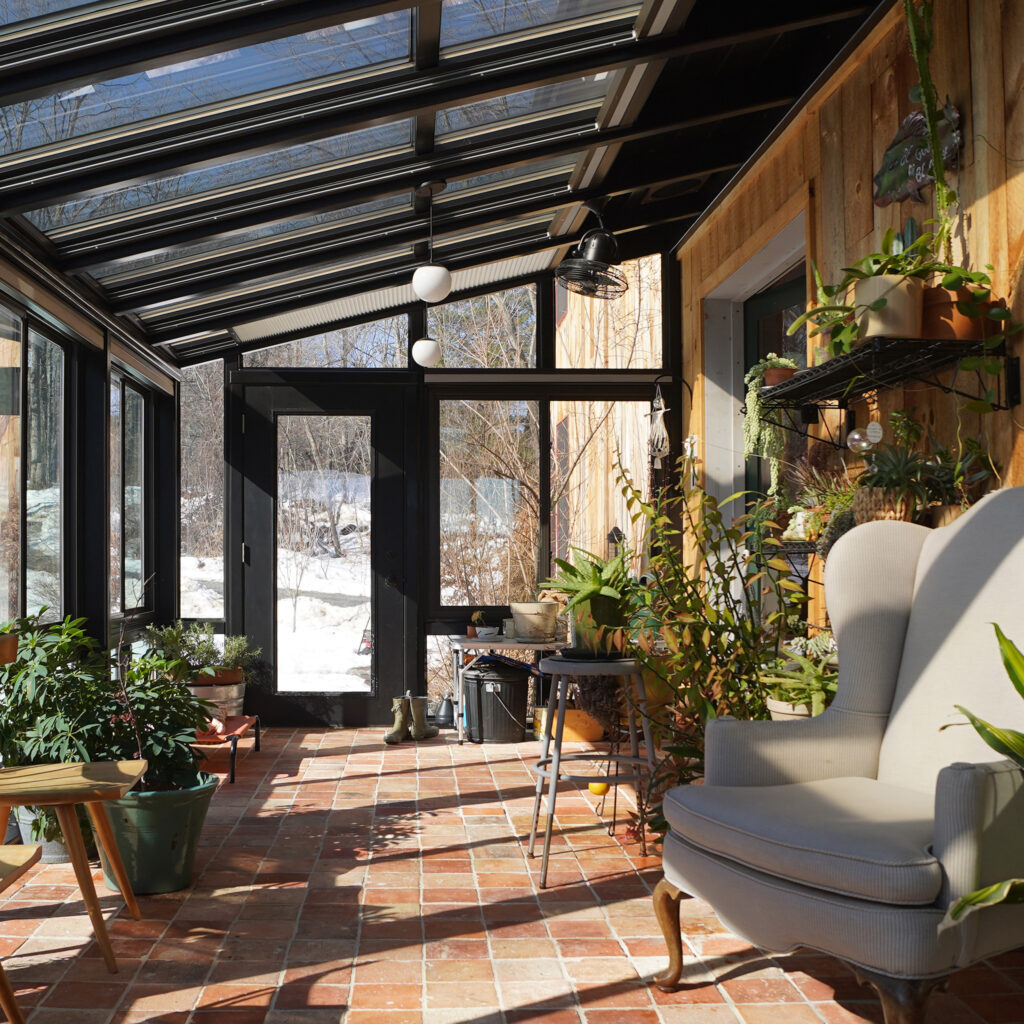 Interior of the sunroom with many plants, chairs, bright lights and windows.